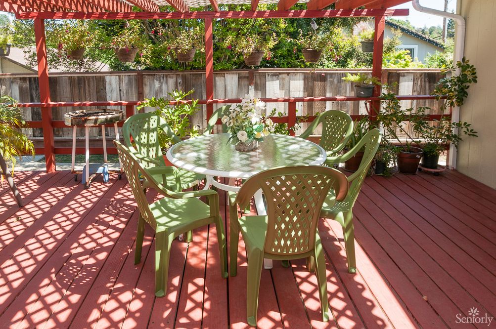 An outdoor patio with a round table and green chairs under a pergola.