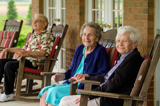 Three elderly women enjoying a moment together on a porch, sharing smiles and companionship.