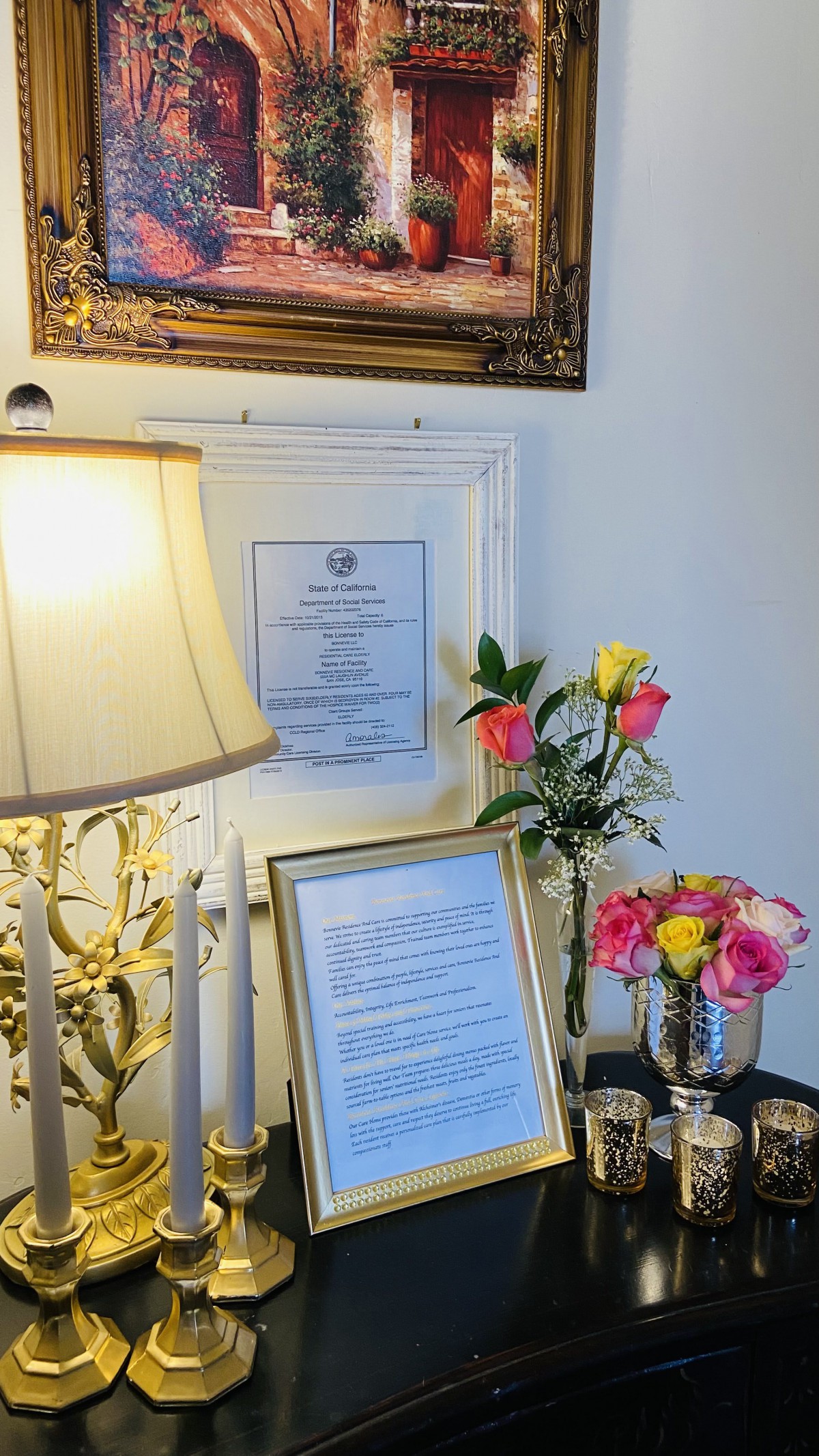 A decorative table setup with a lamp, framed documents, and colorful flowers.