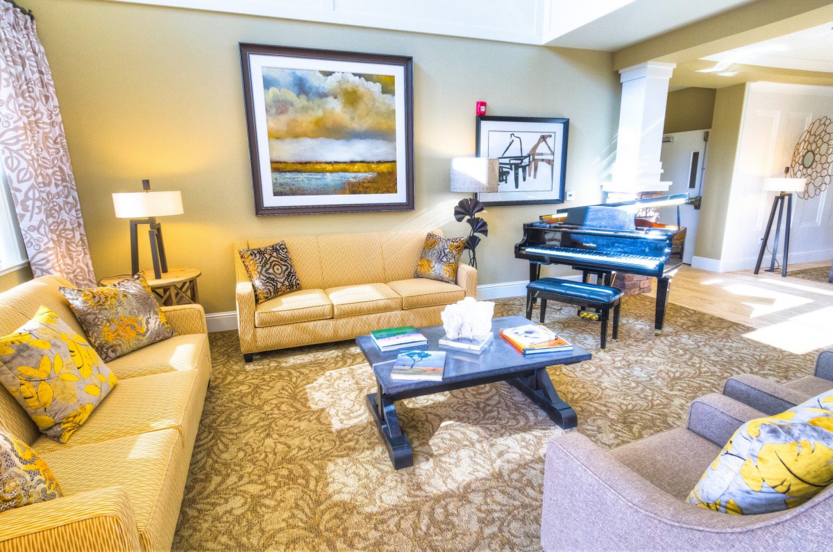 A well-decorated living room featuring beige sofas, a black grand piano, and colorful artwork on the walls.