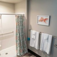 A tidy bathroom featuring a shower with a floral curtain, neatly hung towels, and wall artwork.