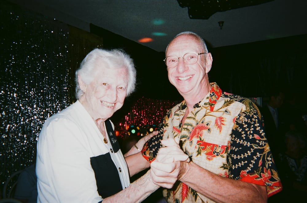 An elderly couple happily dancing together at an indoor celebration.