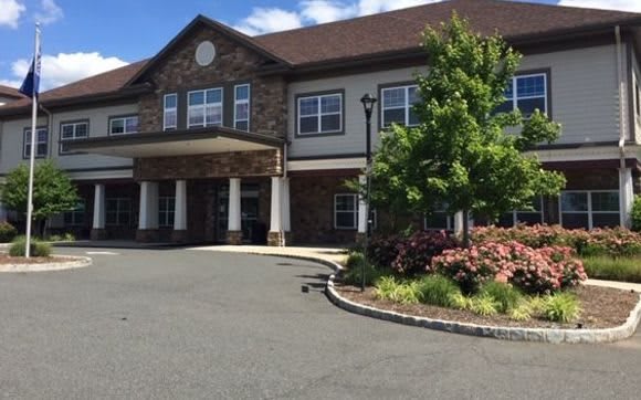 The image shows the exterior of a large building with a landscaped entrance and driveway.
