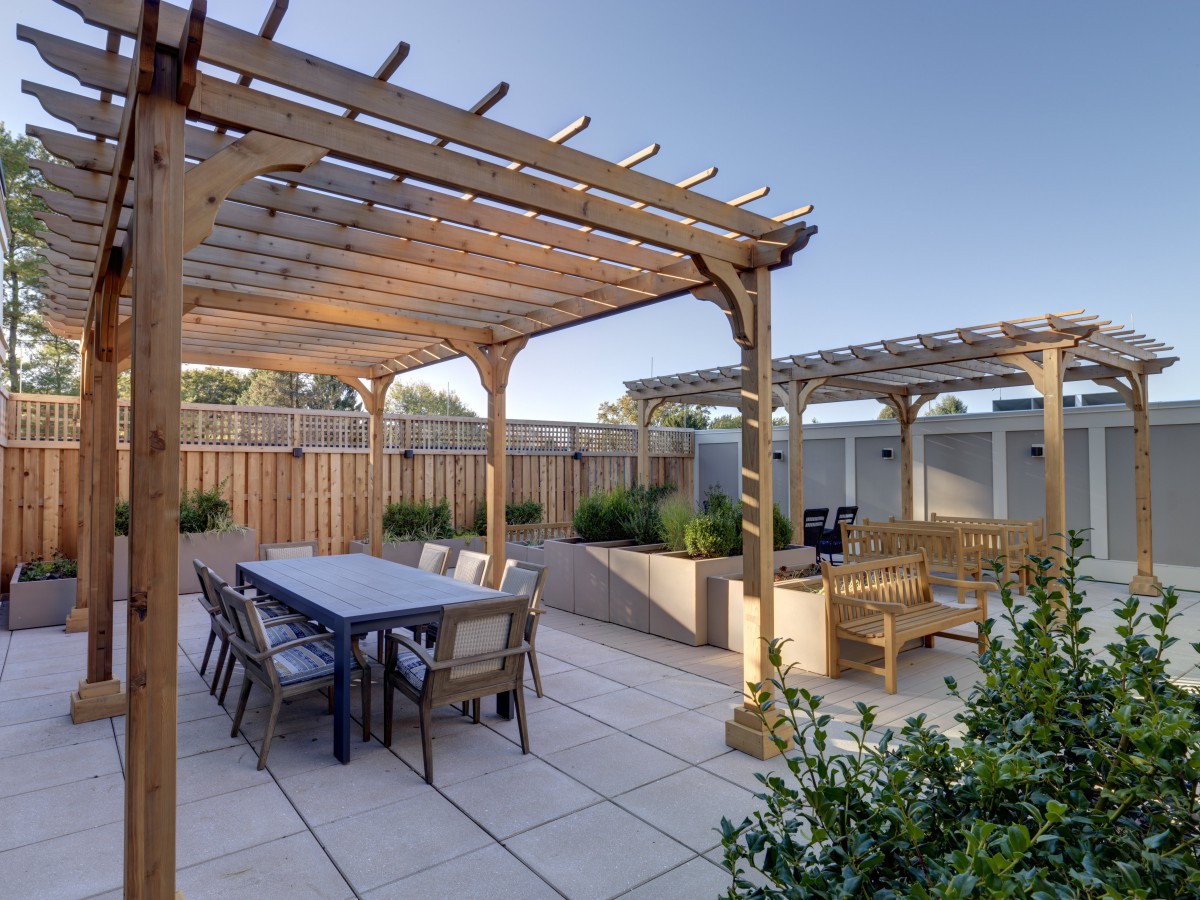 A well-designed outdoor patio with a wooden pergola, dining furniture, and surrounding garden greenery.