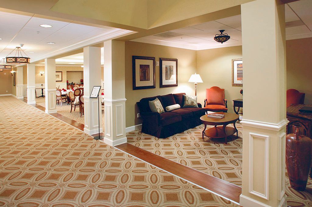 A cozy living room with a sofa, armchair, table, and lamp, complemented by framed artwork and patterned carpet.