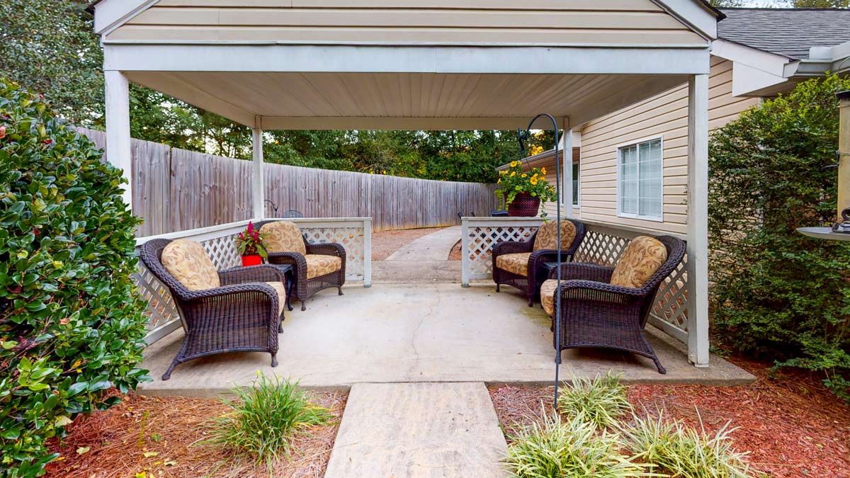 A cozy outdoor patio with wicker furniture under a covered area in the backyard, featuring a garden path and surrounded by a fence.
