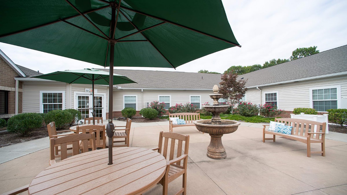 A peaceful patio area with tables, chairs, and large umbrellas surrounding a decorative fountain.
