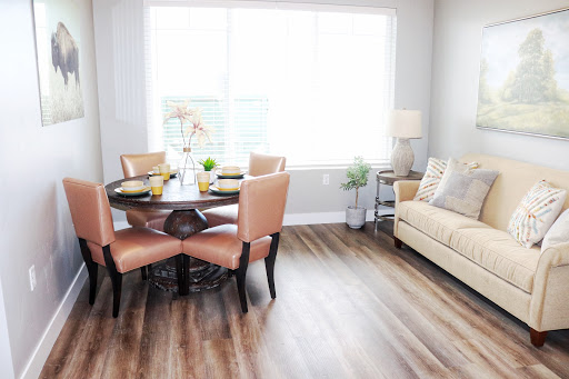 A bright and modern dining area featuring a round table with elegant chairs, complemented by a cozy sofa and natural light from large windows.