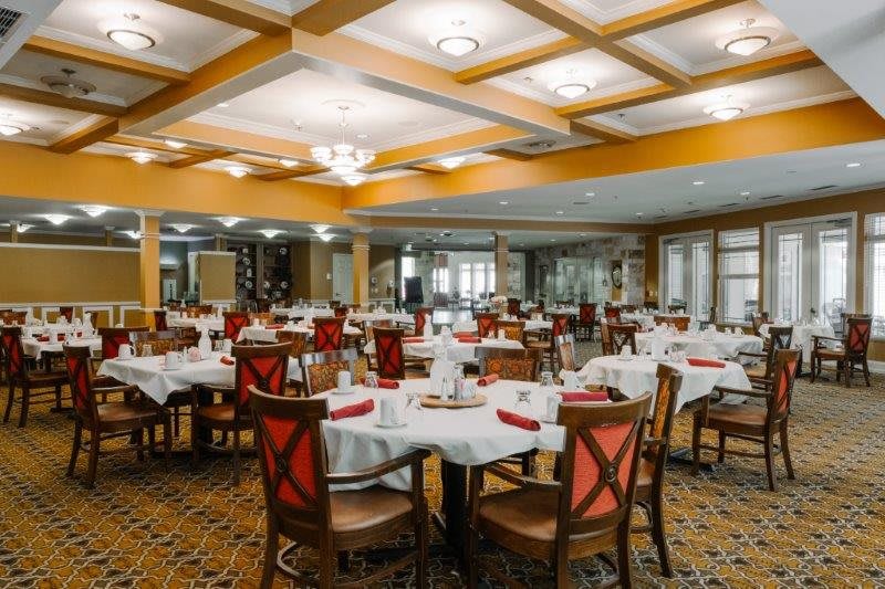 A spacious restaurant dining area with neatly arranged tables and chairs, elegant lighting, and a warm color palette.
