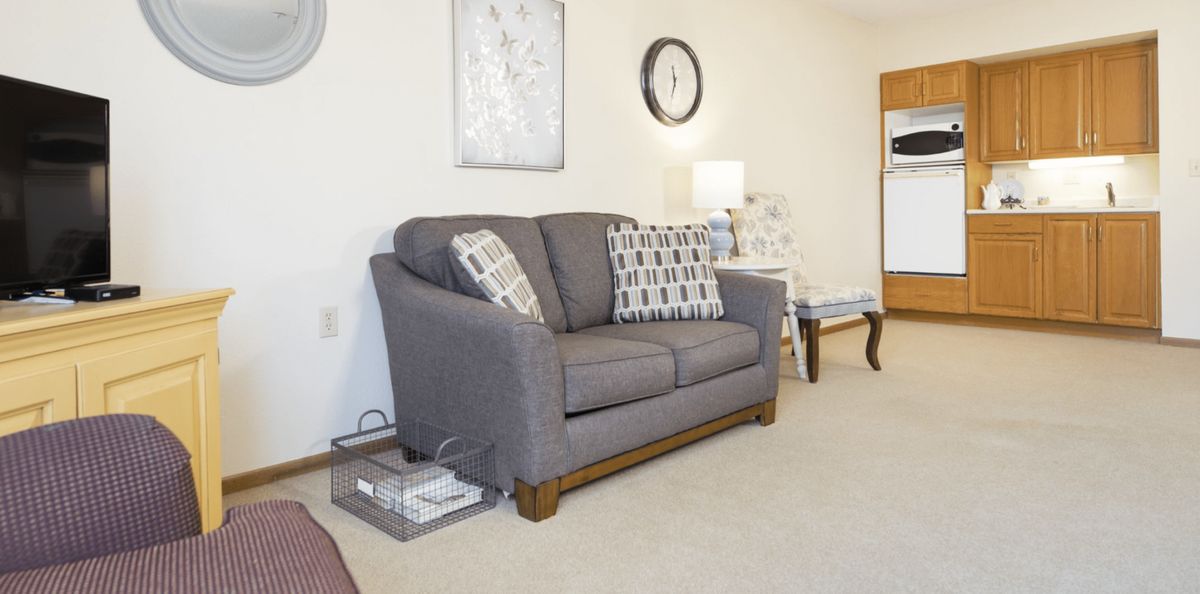 A cozy living room featuring a gray sofa with patterned pillows, complemented by wall decor and a standing lamp.
