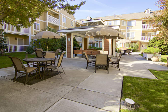 A well-maintained outdoor patio area with tables, chairs, and umbrellas at an apartment complex during the day.