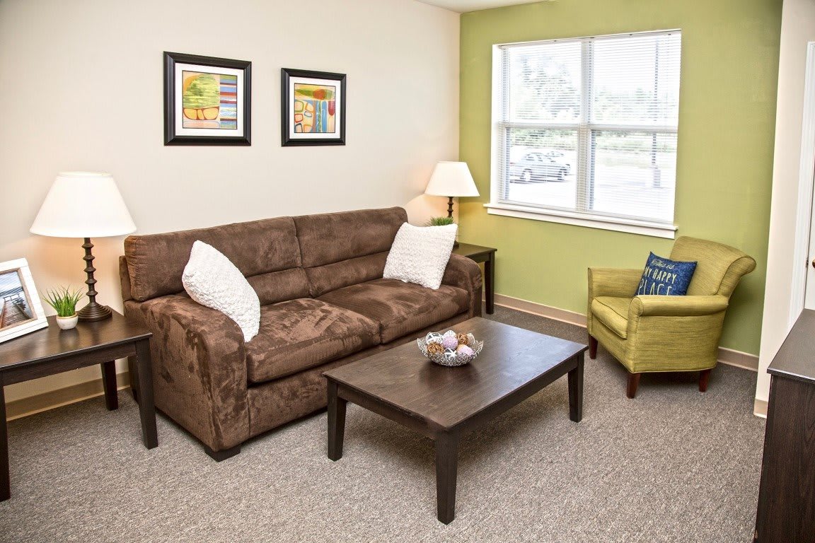 A cozy living room with a brown sofa, green armchair, and a wooden coffee table.