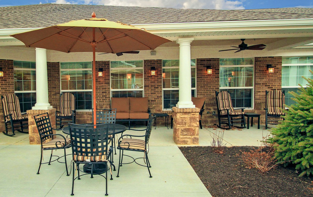 A cozy outdoor patio with a table, chairs, and an umbrella against a brick house.