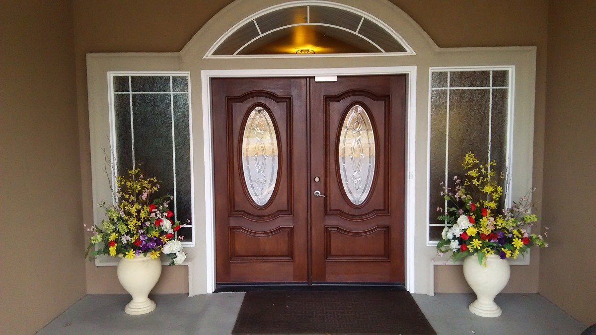 A decorative wooden double door with oval glass panels, flanked by flower pots.