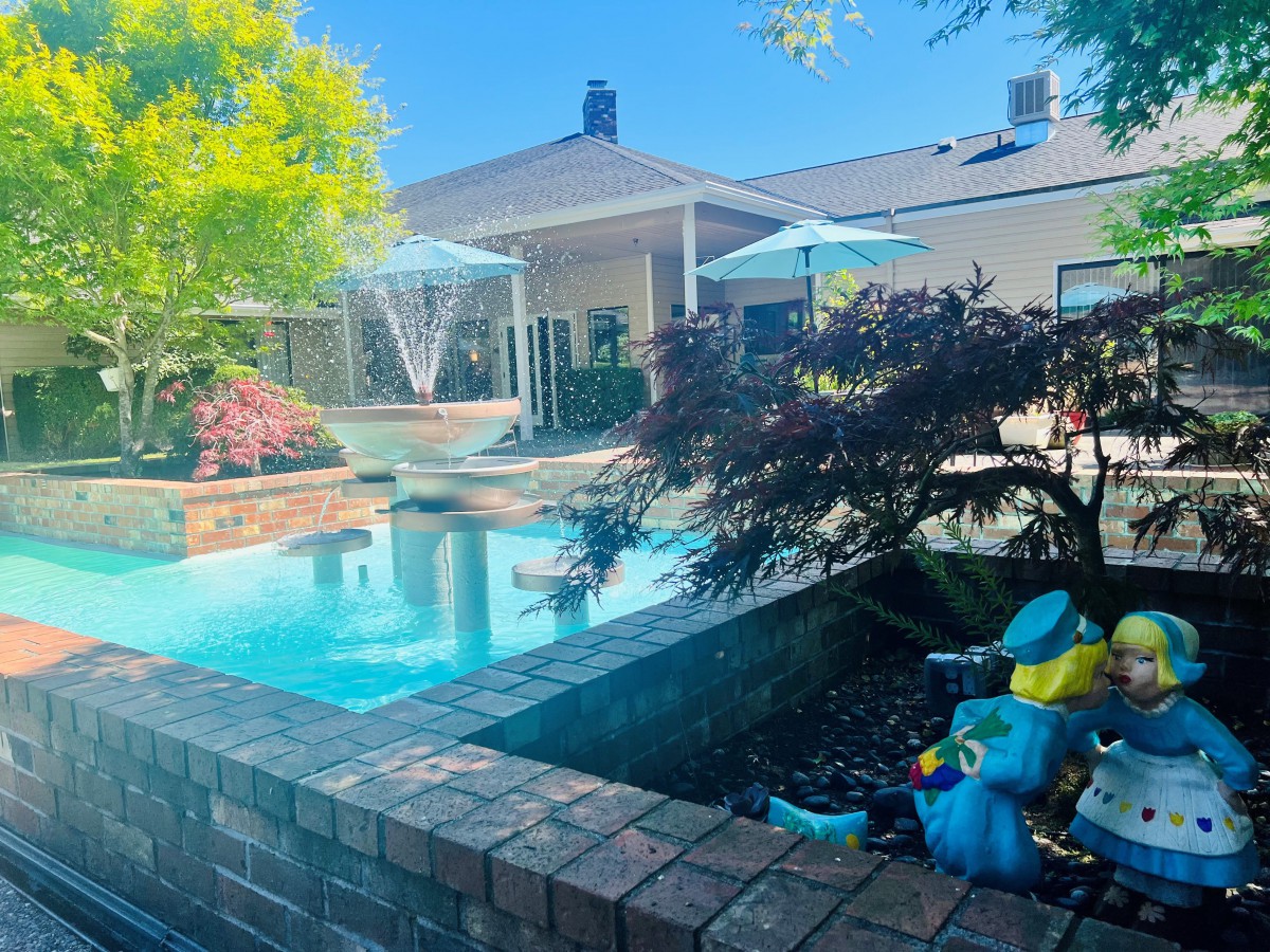 A serene backyard featuring a pool with surrounding greenery and a colorful sculpture.
