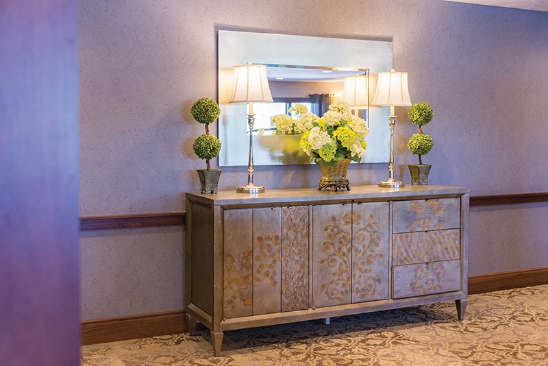 An elegant hallway with a decorative sideboard topped with lamps and flowers in front of a large mirror.