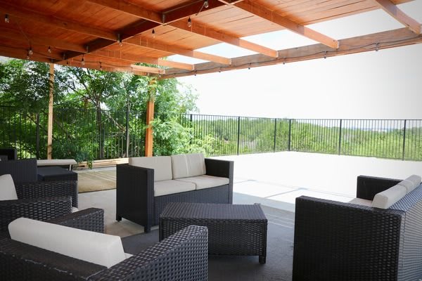 A stylish outdoor patio with modern furniture under a wooden pergola, overlooking a scenic nature view.
