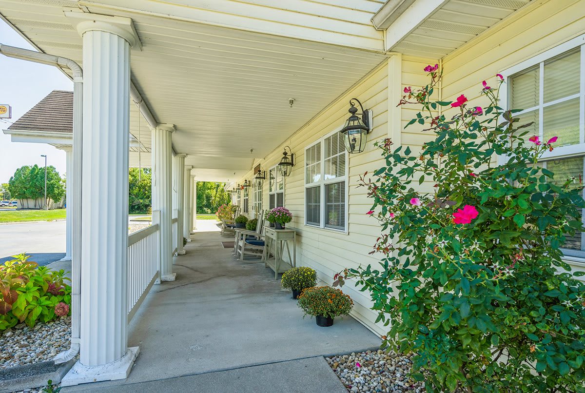 A welcoming porch with white columns, potted plants, and blooming flowers along the building exterior.