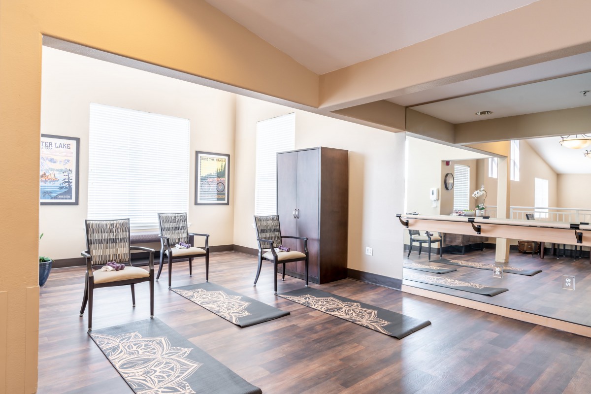 A serene yoga studio with large mirrors, wooden flooring, and neatly arranged chairs and mats.