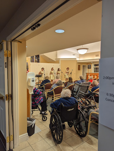 A lively music performance taking place in a senior living community, with residents enjoying the show from their wheelchairs.