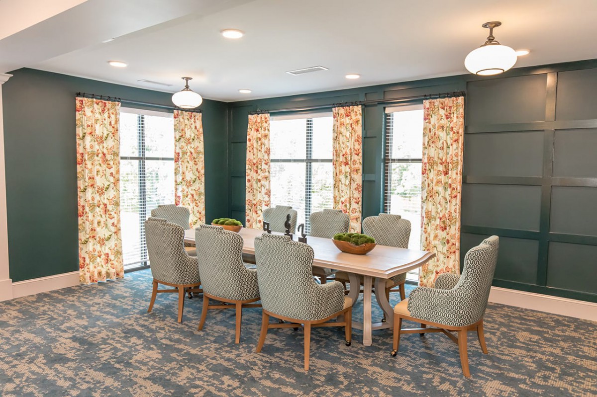 A well-decorated dining room featuring a large table with upholstered chairs, floral curtains, and ample natural light.