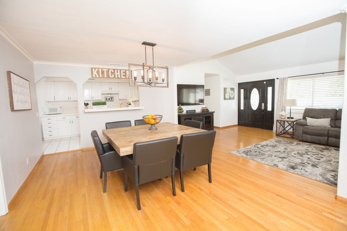 A modern dining room with a wooden table and chairs set on a polished wooden floor, leading into an open kitchen area.