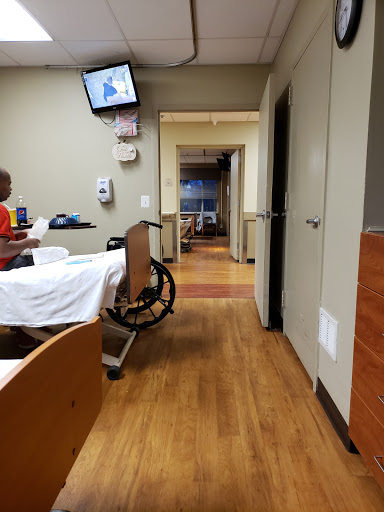 A view of a hospital patient room, featuring a wheelchair and an empty bed.