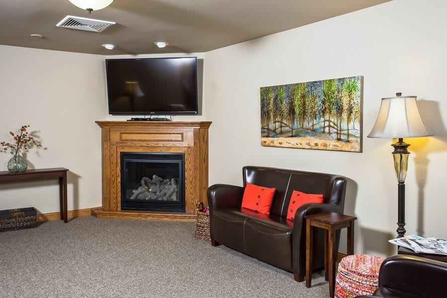 A cozy living room featuring a fireplace with a television mounted above, accompanied by a leather sofa and decorative artwork on the wall.