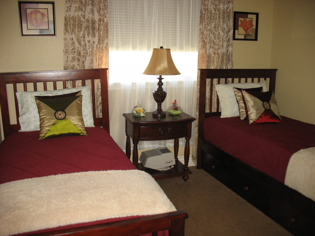 A cozy bedroom featuring two twin beds with decorative pillows, a central nightstand with a lamp, and wall art.