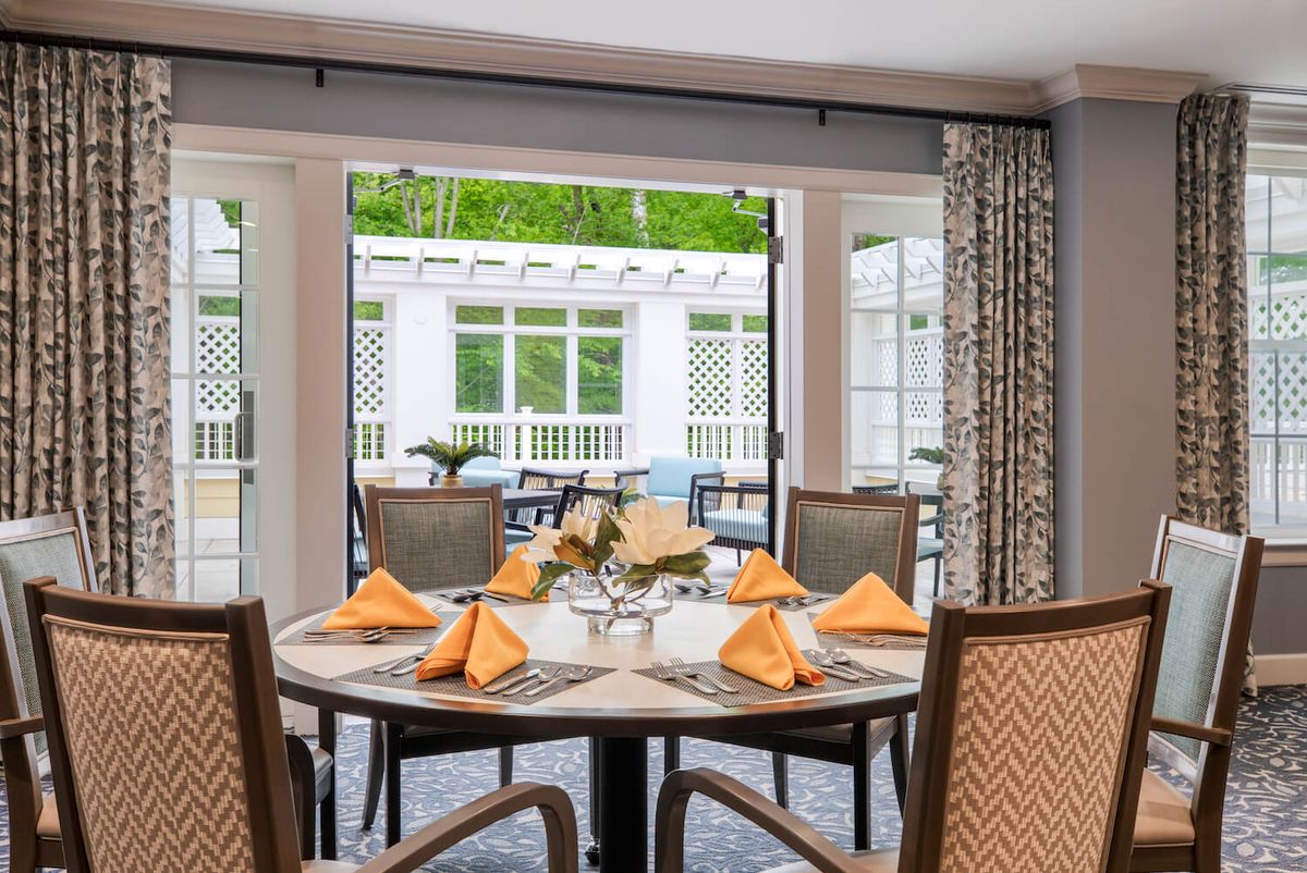 A well-set dining table with orange napkins, situated near glass doors overlooking a patio.