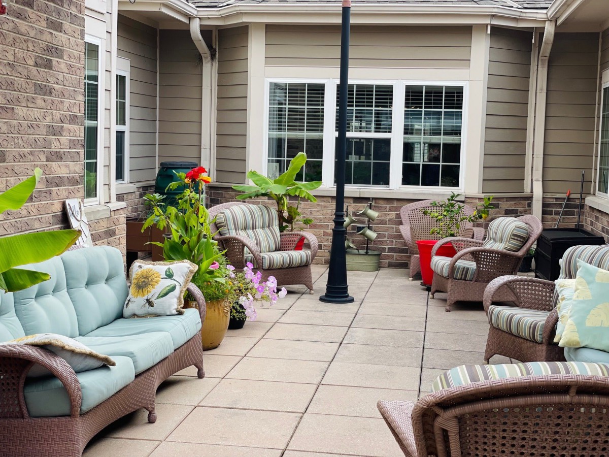 A cozy patio with wicker furniture and colorful cushions surrounded by potted plants.