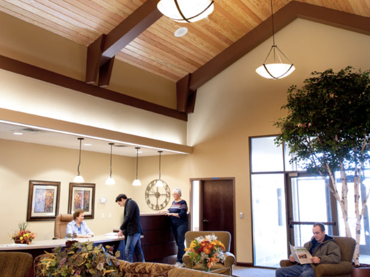 A modern reception area with people interacting at a desk and others seated in the waiting area.