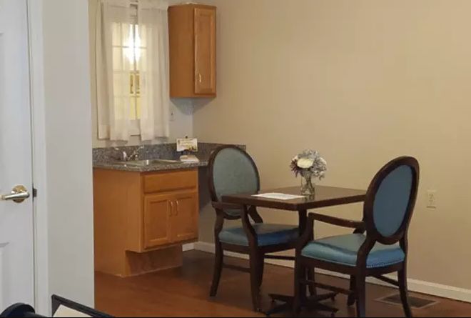 A cozy dining area with a small table, two chairs, and a kitchenette in the background.