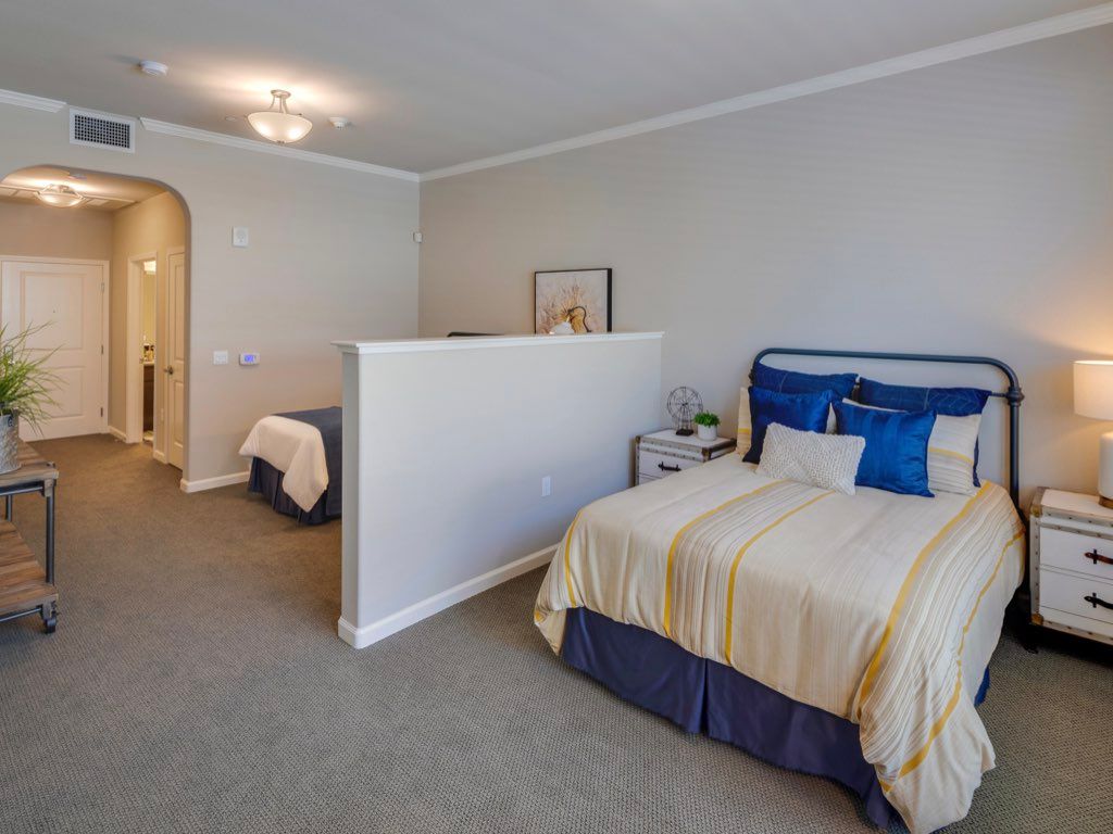 A spacious bedroom featuring a double bed with blue and beige bedding, separated by a partial wall.