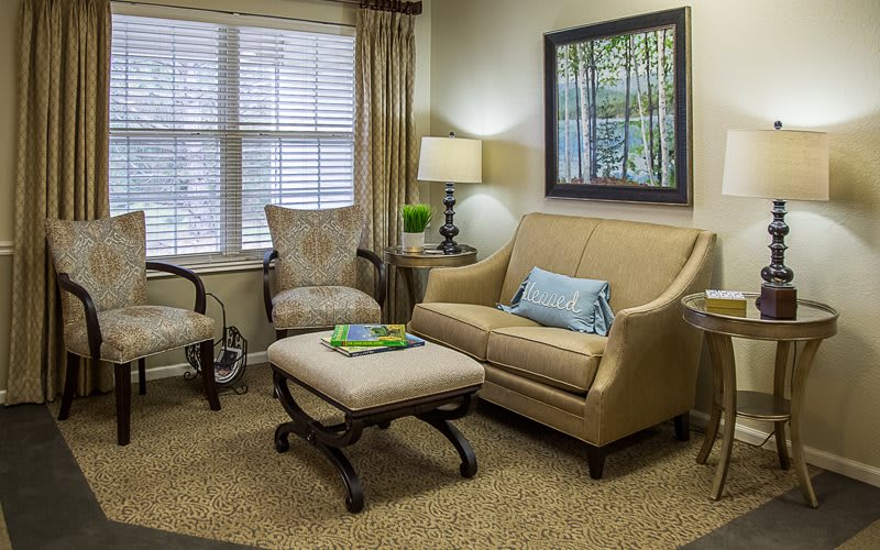 A cozy living room with neutral-toned furniture and decor, featuring a sofa, armchair, lamp, and artwork on the wall.