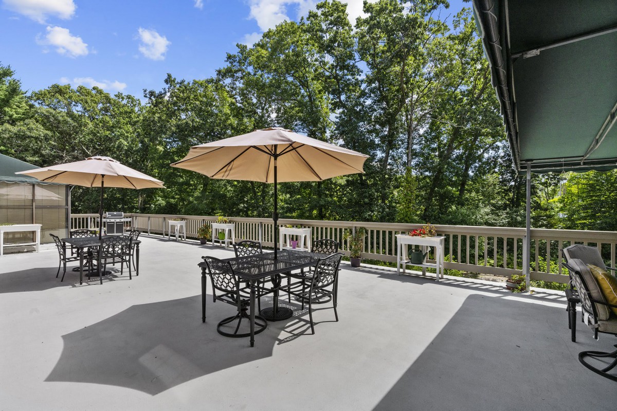 A spacious outdoor patio area with tables, chairs, and umbrellas, surrounded by lush trees.