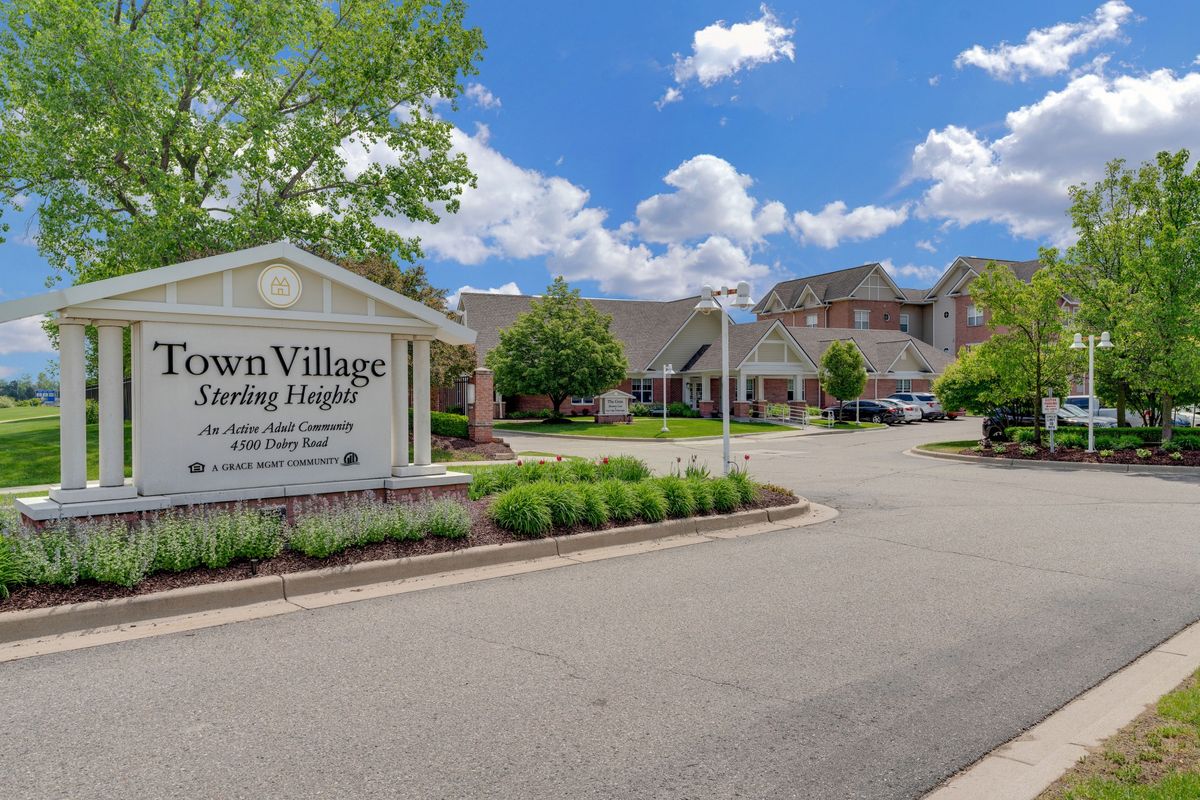 Entrance to a senior living community with a sign and landscaped driveway.