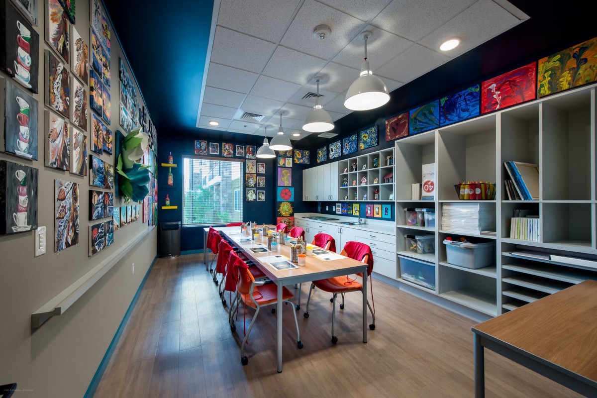 A colorful art classroom featuring tables, chairs, and organized shelves filled with supplies.