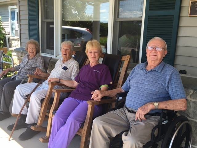 A group of elderly people sitting on rocking chairs on a porch, enjoying each other's company.
