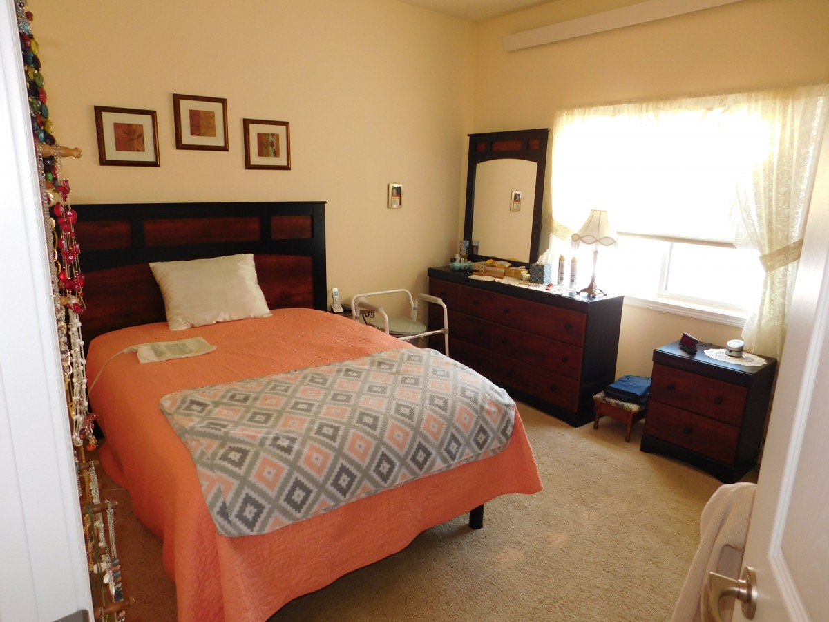 A cozy bedroom with a single bed covered in orange bedding, accompanied by a dresser and a window letting in natural light.