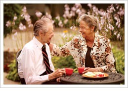 An elderly couple enjoying coffee and conversation outdoors.