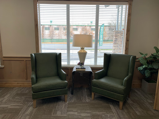 A cozy seating arrangement featuring two green armchairs and a lamp by the window.