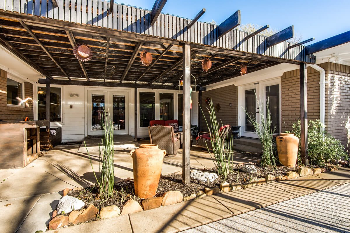 A charming outdoor patio featuring a pergola with terracotta pots and plants, creating a shaded seating area.