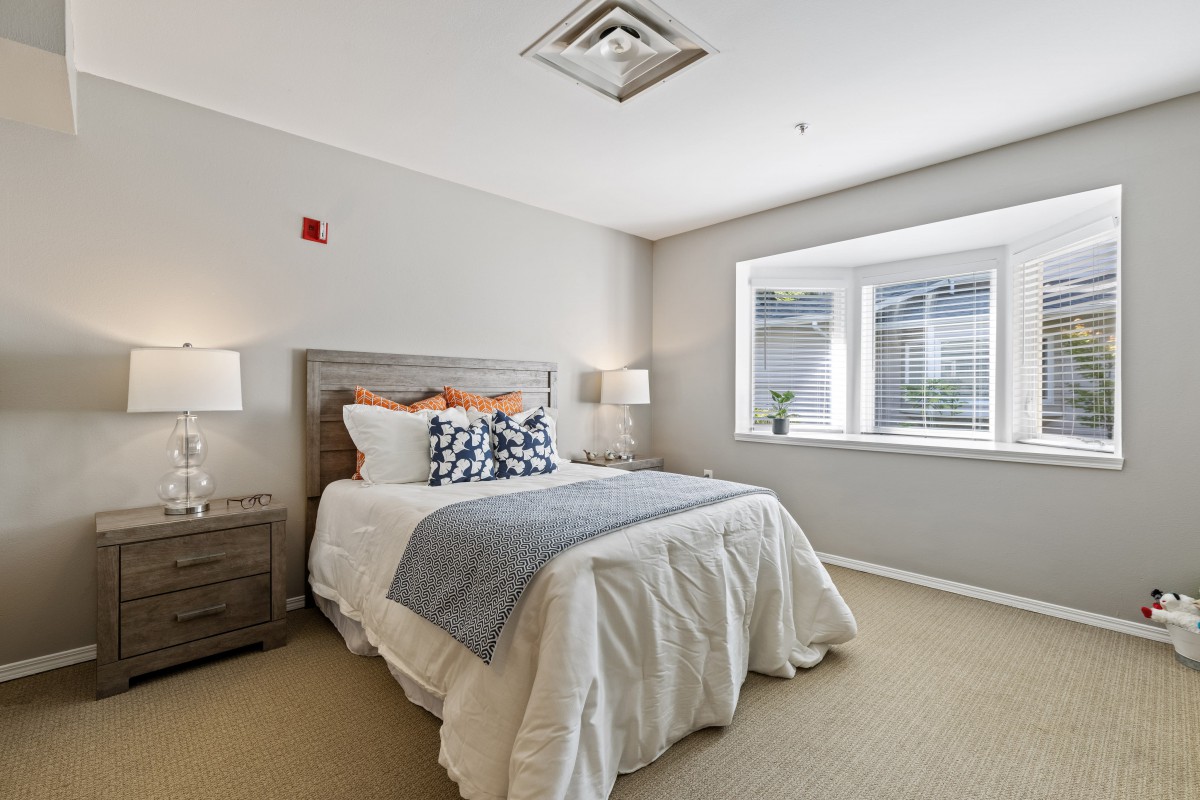 A cozy bedroom with a neatly made bed, bedside tables, and a large window.