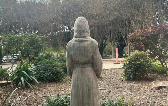 A statue in a garden surrounded by greenery and trees.