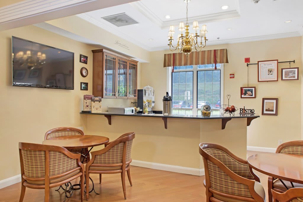 Cozy dining area with wicker chairs and tables, featuring a counter with a coffee maker and a mounted television.