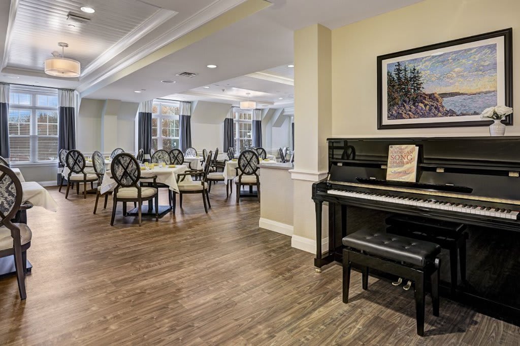 A spacious dining room with elegant seating, featuring a piano and artwork on the wall.