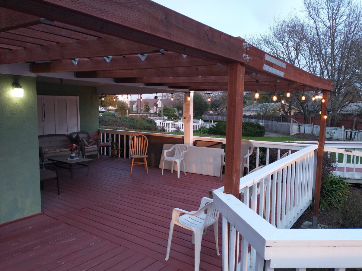 A cozy outdoor deck featuring a pergola, string lights, and seating areas in a residential setting.