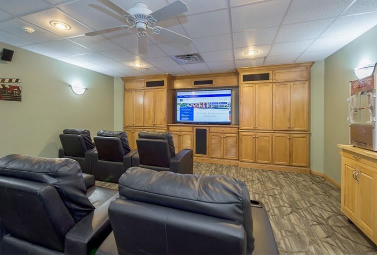 A cozy home theater setup with leather recliners facing a large screen surrounded by wooden cabinetry.