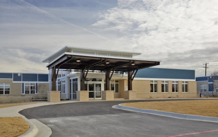 A modern building with a prominent entrance and a cloudy sky overhead.